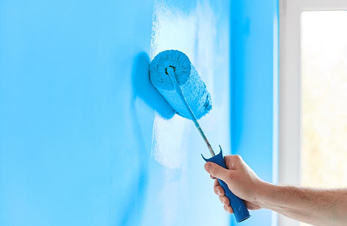A worker brushing blue paint onto the wall 
